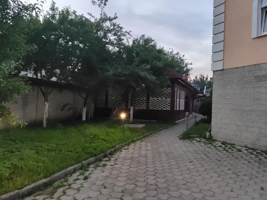 Дорожка к беседке из плитки с горящими фонариками по обеим сторонам. Виден угол дома.