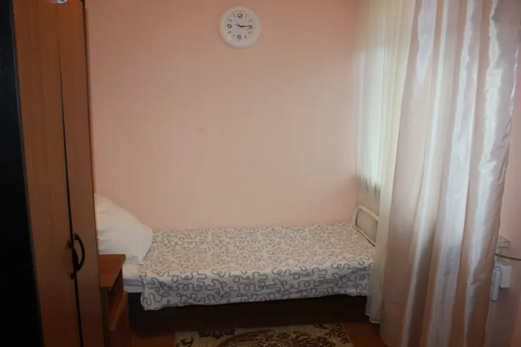 В комнате виден шкаф, кровать и окно со светлыми зановесками